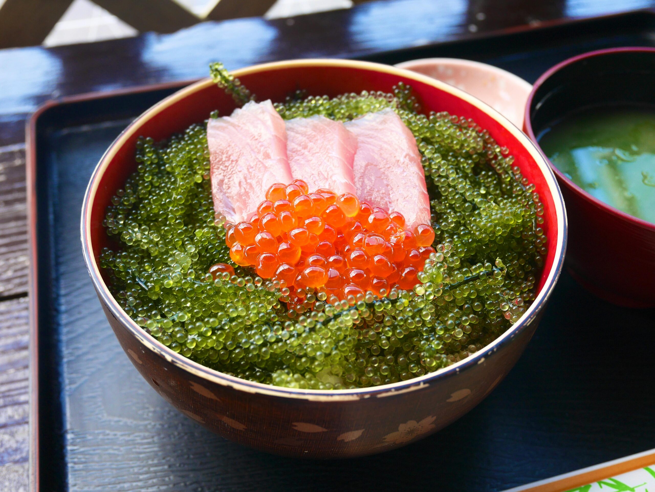 High angle of bowl with sashimi with red caviar and tobiko placed on wooden tray