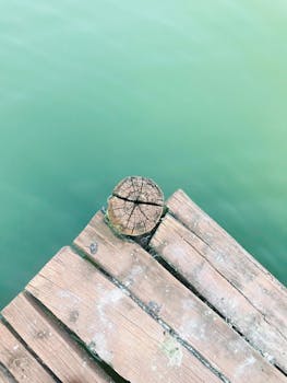 Close-up of a rustic wooden dock extending over serene green water in Kadarkút, Hungary.