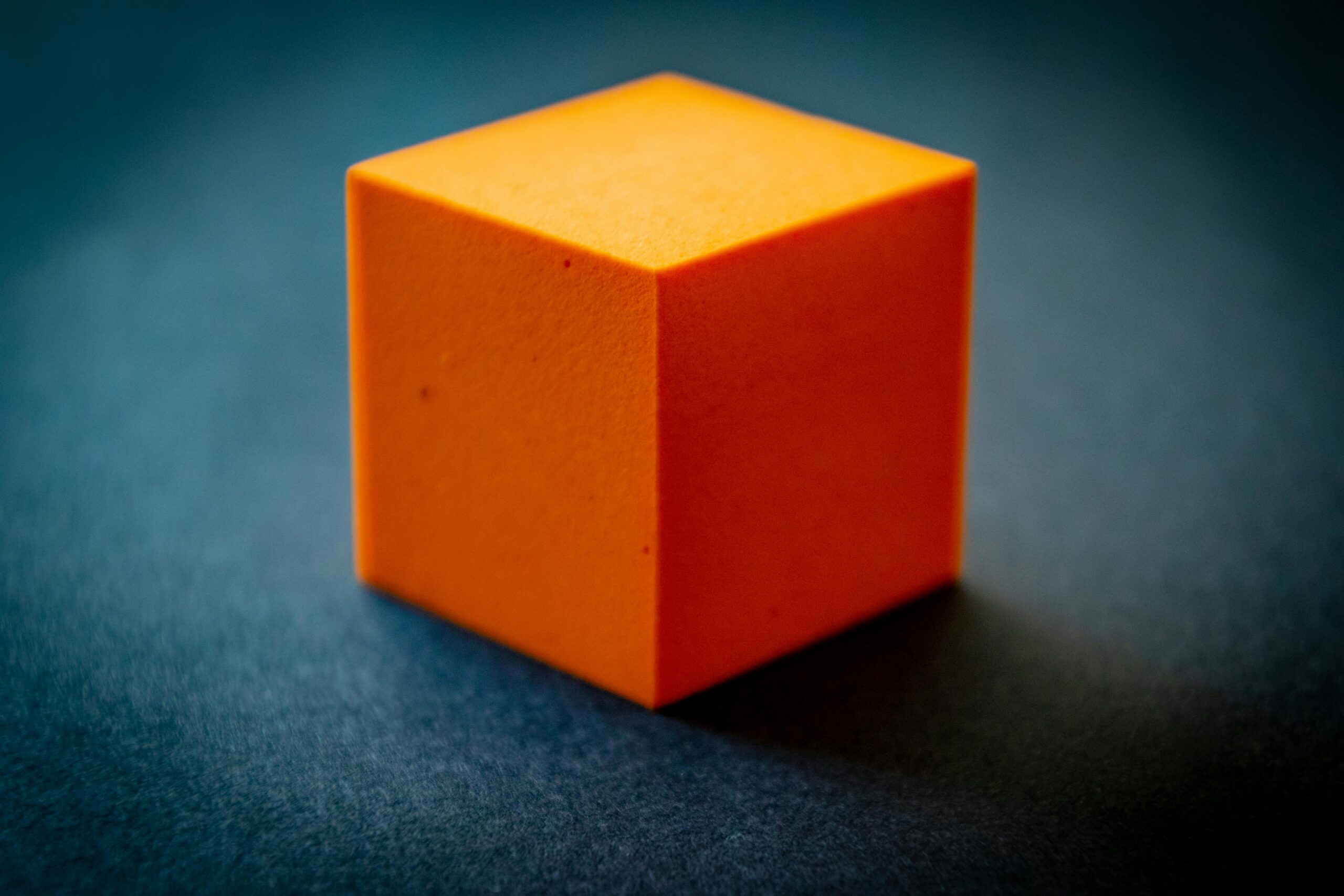 Close-up of an orange foam cube on a dark surface, highlighting its texture and color contrast.