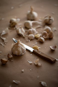 A close-up of garlic cloves and a wooden knife on a rustic brown surface, showcasing a warm and earthy kitchen setting.