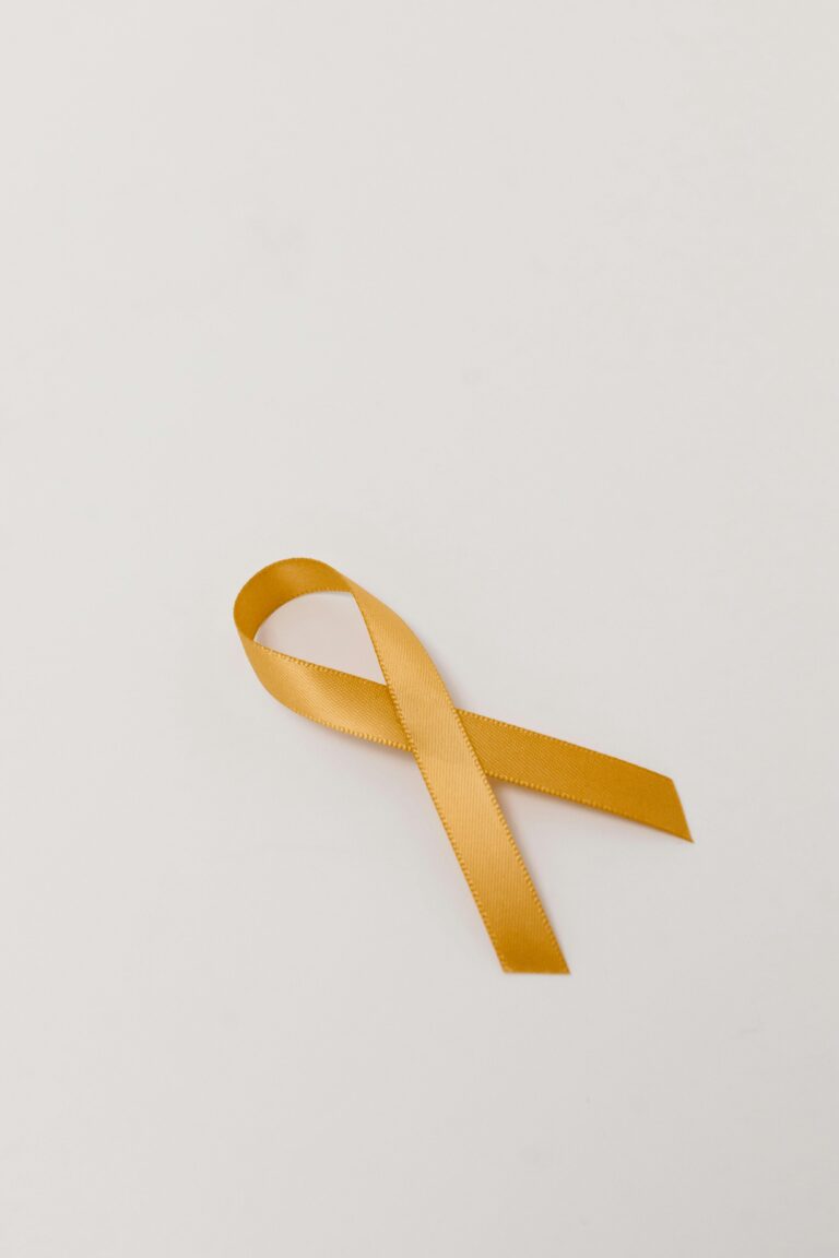 A close-up of a gold awareness ribbon on a white surface symbolizing cancer awareness and support.