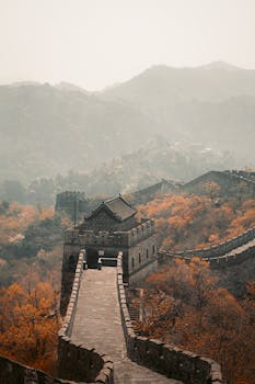 Scenic view of the Great Wall of China surrounded by autumn foliage and foggy mountains.