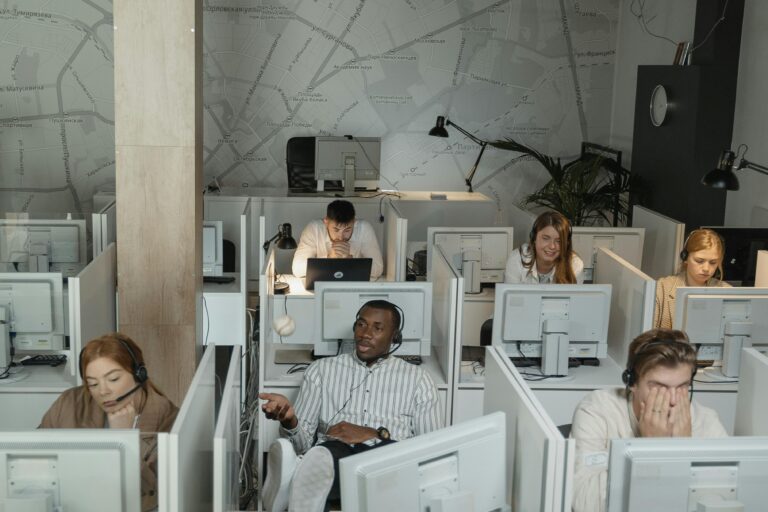 A group of diverse call center employees working with computers and headsets in cubicles.