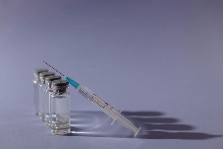 Syringe and vaccine vials arranged on gray surface, symbolizing healthcare and immunization.