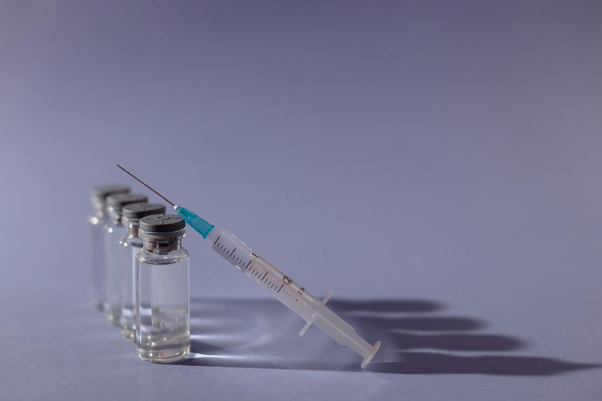 Syringe and vaccine vials arranged on gray surface, symbolizing healthcare and immunization.
